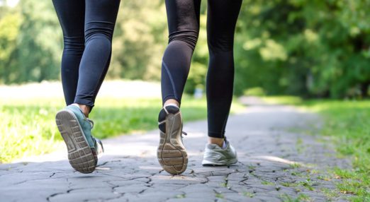 Two people, shown from behind and legs only, walking on a park path, wearing black leggings and trainers