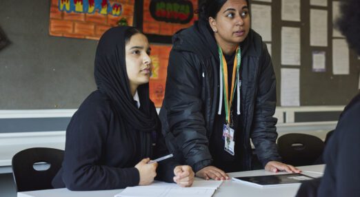 A counsellor stands next to a girl in a classroom
