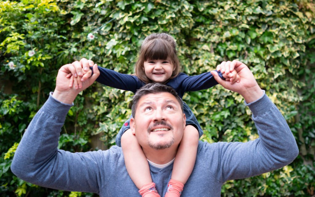 A man holding a young girl on his shoulders, looking up