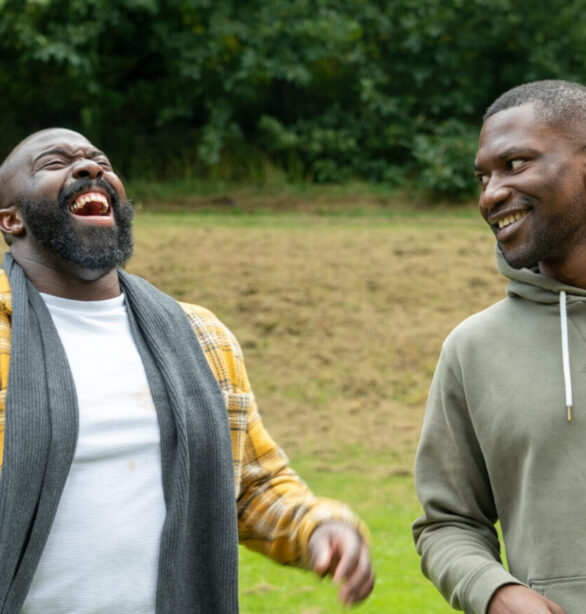 Two men walking together outdoors, one laughing, the other smiling