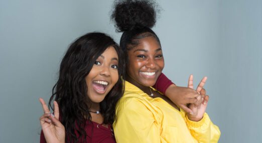 Two young women, smiling and holding up two fingers in excitement