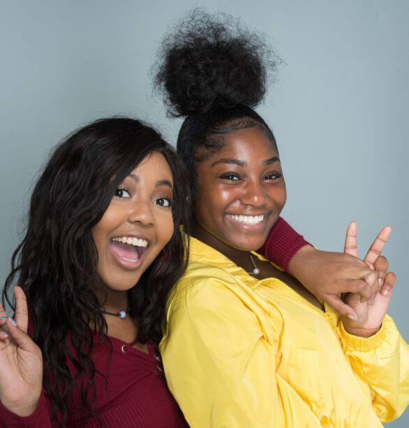Two young women, smiling and holding up two fingers in excitement