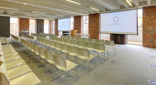 A meeting room at ORTUS with rows of chairs set out, looking towards a lectern and projector screen