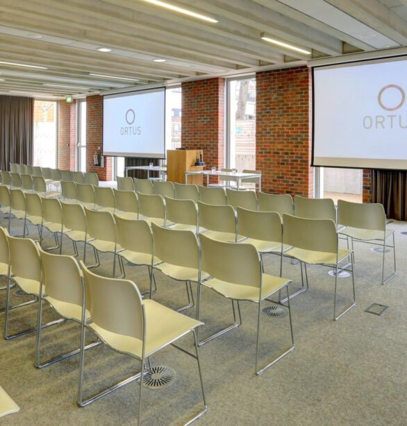 A meeting room at ORTUS with rows of chairs set out, looking towards a lectern and projector screen