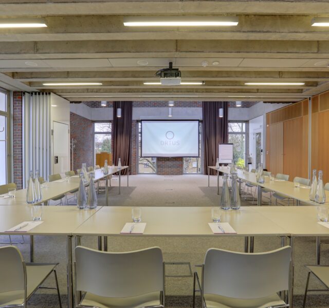 Tables and chairs laid out in a large U shape, with a projector and screen at the far end