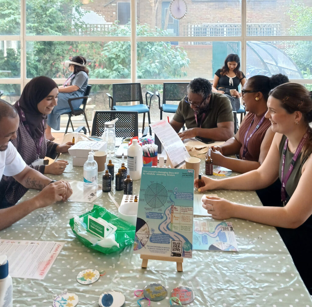 A small group of men and women, seated around a table, making something each and talking together