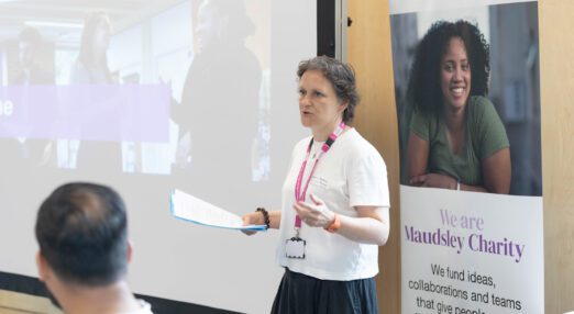 A woman stands in front of a screen, speaking to a meeting