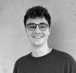 Portrait of Oran, a smiling man standing in front of a plain background