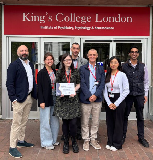 A small group of 7 people, standing outside the doors of King's College London, holding a certificate proudly