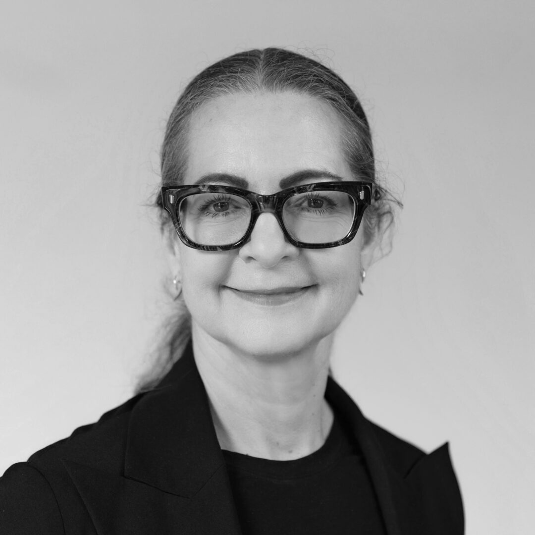 Portrait of a woman, wearing glasses, looking directly towards the viewer, smiling