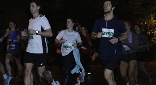 Several people running in the dark, each wearing a running bib with a number