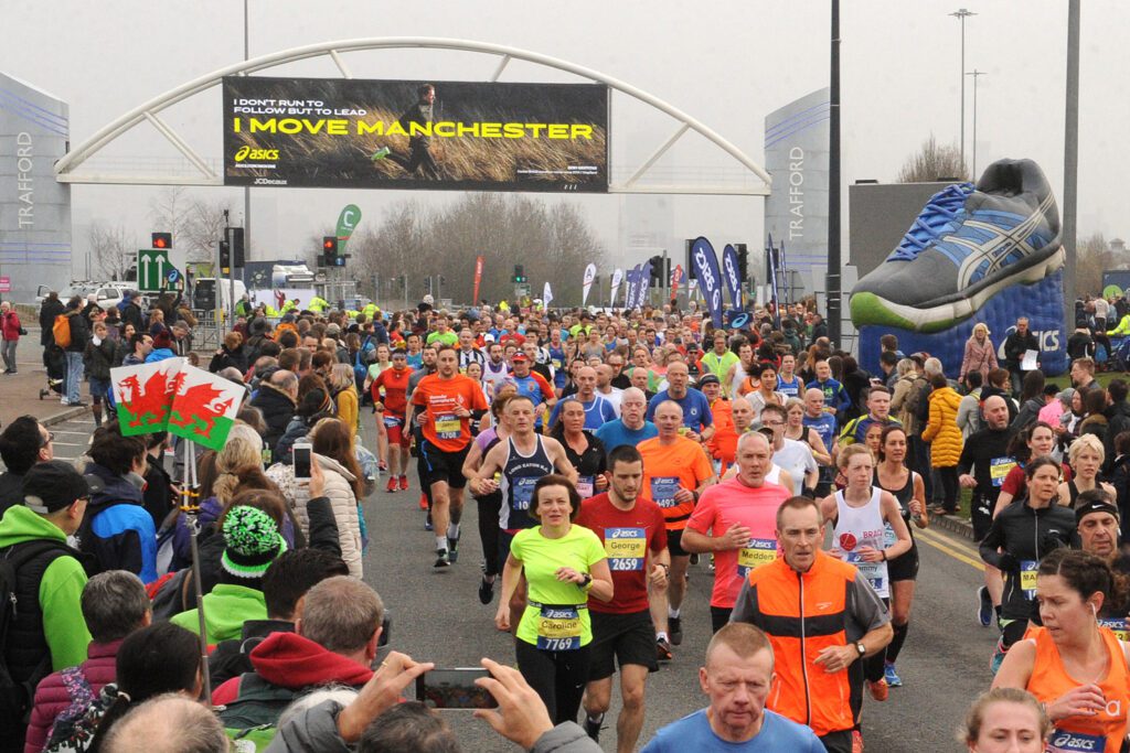 Runners heading along a road, surrounded by supporters and a sign is in the background that reads "I move Manchester"