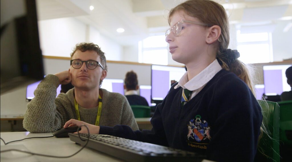A girl using a computer, with a young man looking on
