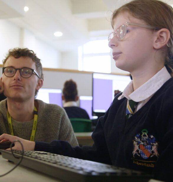 A girl using a computer, with a young man looking on