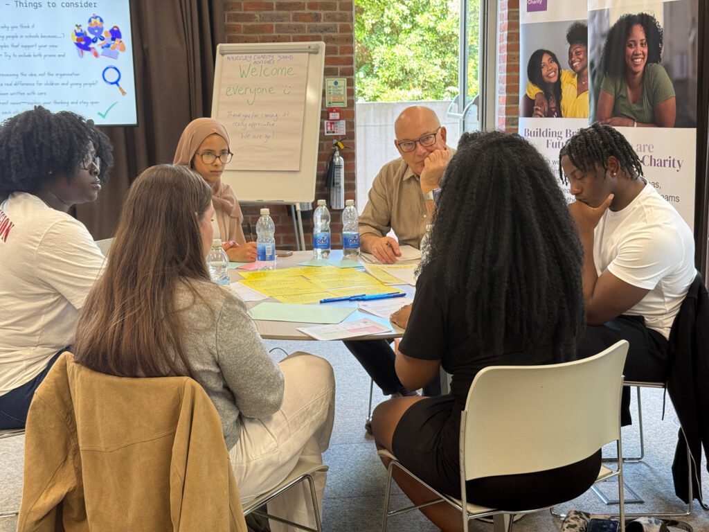 Four young people seated at a table with a man, writing on sheets of paper and in the middle of a discussion