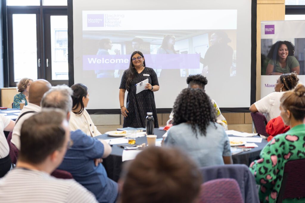 An asian woman standing in front of a room of seated people, smiling as she speaks