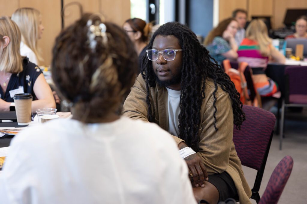 Two people, a black man and woman seated in an event, speaking together.