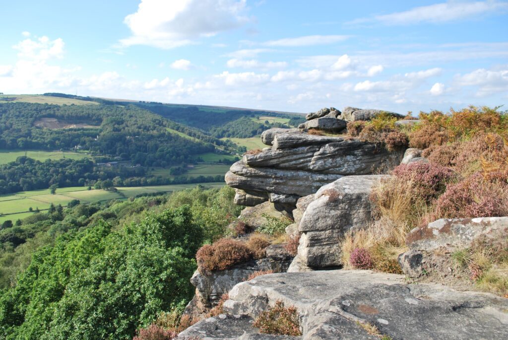 The view from on top of a hill with large rocky outcrops, looking down over a green valley of trees and fields