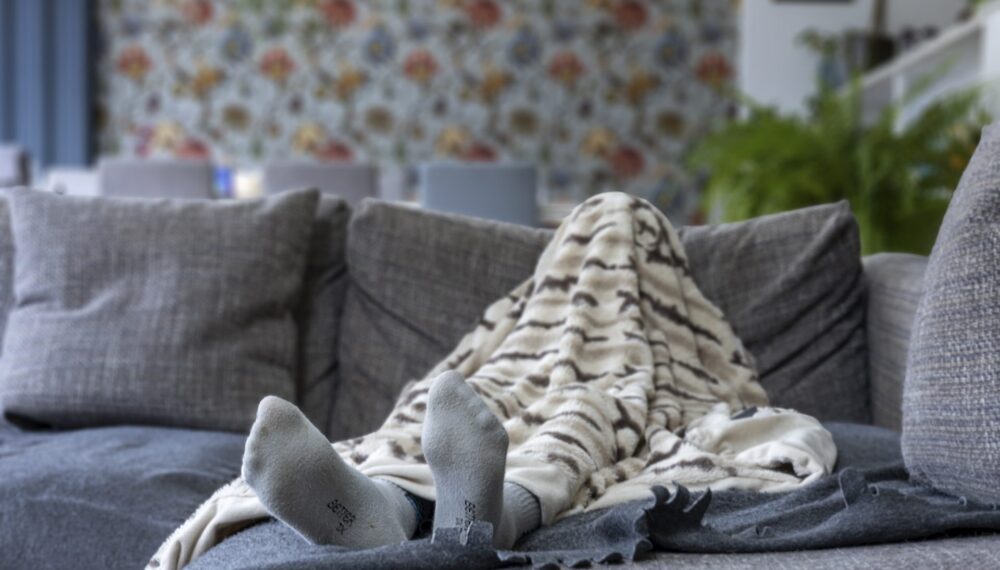 A child's foot is visible under a patterned duvet, located on a sofa, the child is hidden under the duvet