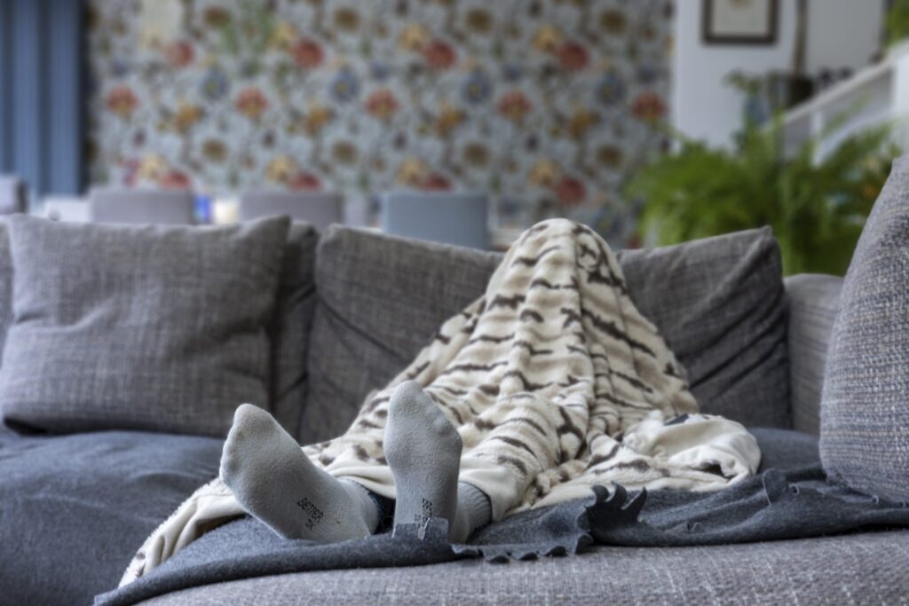 A child's foot is visible under a patterned duvet, located on a sofa, the child is hidden under the duvet