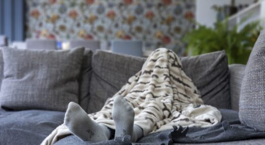 A child's foot is visible under a patterned duvet, located on a sofa, the child is hidden under the duvet