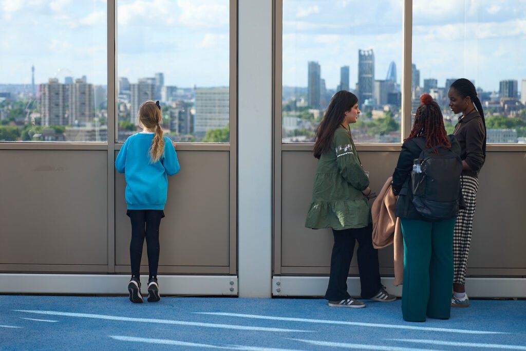 Three girls standing outdoors on a patio space with a view across London