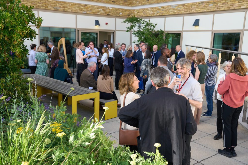 An external garden and patio space filled with people chatting together.