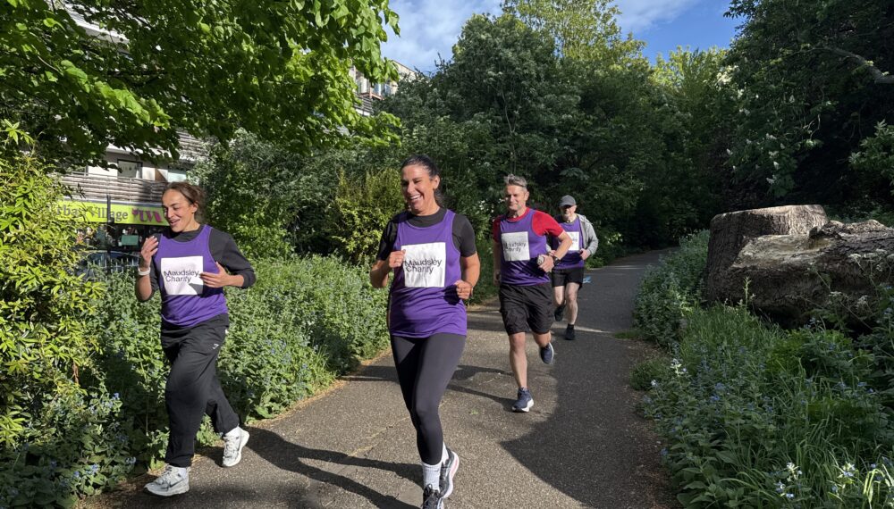 Four people running together through a park, three people are wearing purple Maudsley Charity running tops, showing the logo