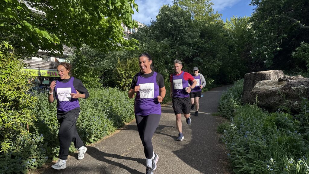 Four people running together through a park, three people are wearing purple Maudsley Charity running tops, showing the logo