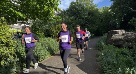 Four people running together through a park, three people are wearing purple Maudsley Charity running tops, showing the logo